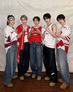 Five TXT K-pop group members posing together in red and white outfits with baggy jeans
