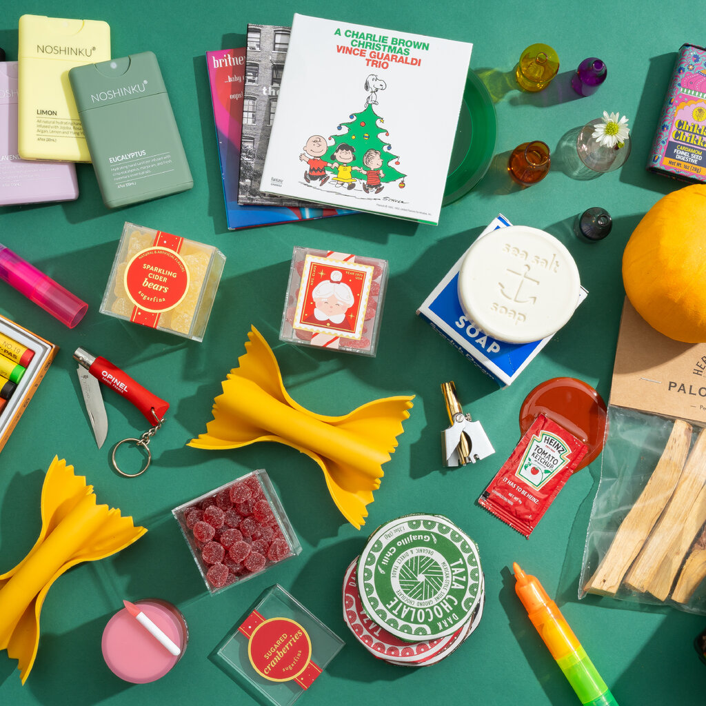 Flat lay of assorted stocking stuffer gifts, candy, notebooks, pens, and small festive items on teal