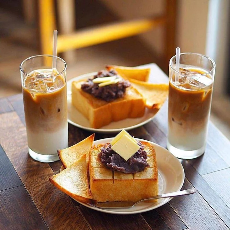 Two iced lattes with thick toast topped with red bean paste and butter on a cafe table