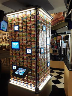 Tall illuminated display tower stacked with rows of colorful Spam cans in an indoor retail or museum space