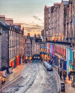 Wet curved street in Edinburgh lined with stone buildings and colorful shopfronts at sunset