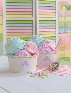 Pink and blue ice cream scoops in pastel rainbow cups with colorful sprinkles on white table