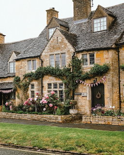 Historic English stone cottage with climbing plants, flowers, slate roof, and decorative bunting