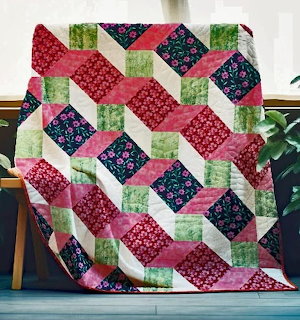 Colorful patchwork quilt with red, green, and navy floral squares in a diagonal pattern draped over a chair