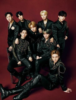 Seven young men in black outfits posing together in a studio with a dark red background