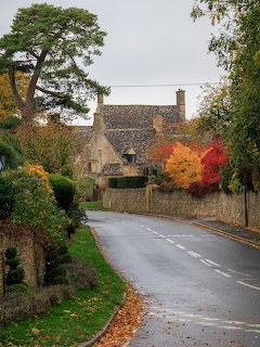 Curving village road with stone cottage and autumn trees on a rainy day