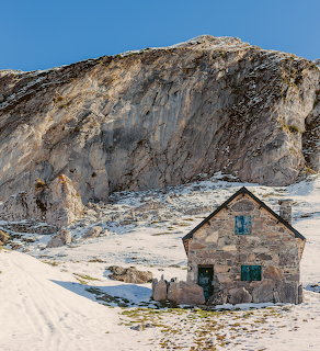 Stone house in snowy mountain terrain with rocky cliff backdrop