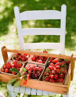 Wooden carrier basket filled with fresh strawberries in punnets on a white wooden chair outdoors