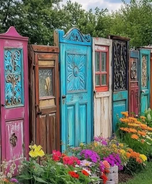 Row of colorful vintage wooden doors standing upright in a garden with flowers in front