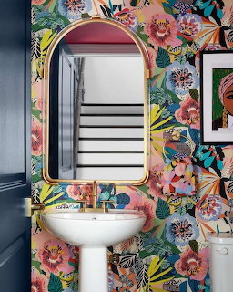 Bathroom with colorful floral wallpaper, white pedestal sink, and coral oval mirror