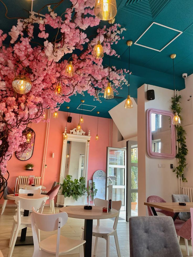 Cafe interior with pink cherry blossom decor, pendant lights, teal ceiling, and pastel pink walls