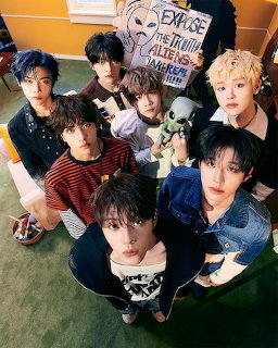 Seven young men posing together looking up at camera in a green room with alien decoration