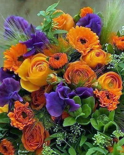 Colorful bouquet with orange, yellow, and purple flowers including ranunculus, roses, and anemones with greenery