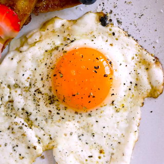 Overhead view of a fried egg with bright orange yolk, seasoned with pepper and herbs on a white plate