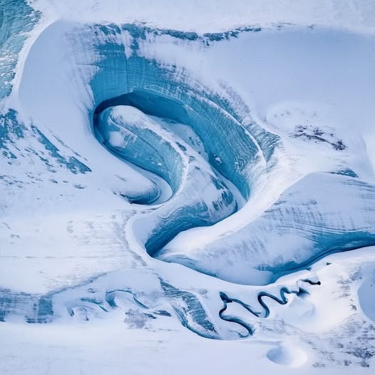 Aerial view of winding blue meltwater channels curving through white ice and snow