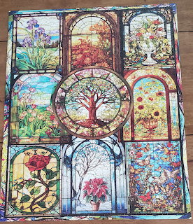Completed jigsaw puzzle with nine stained glass window panels showing trees, flowers, and seasonal nature scenes