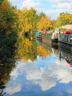 Narrowboats on a calm canal lined with autumn trees, reflections on the water