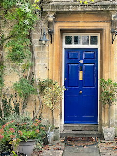 Bright blue front door with transom windows in a honey stone building entrance flanked by potted plants
