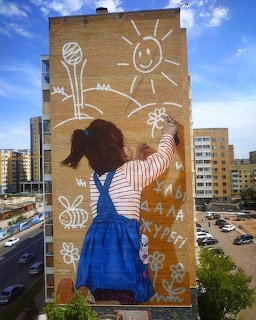 Street art mural on building showing a girl in denim overalls drawing a sun and flowers on the wall