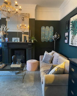 Elegant living room with beige sofa, black fireplace, chandeliers, and framed artwork