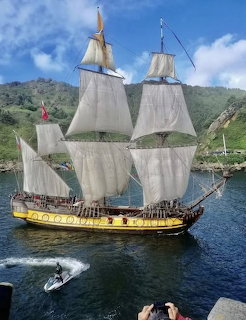 Traditional tall ship with white sails on blue water near green hills