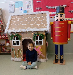 Young girl sitting by a gingerbread house prop and large nutcracker indoors