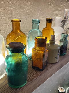 Collection of vintage glass bottles in green, amber, and blue on a wooden shelf