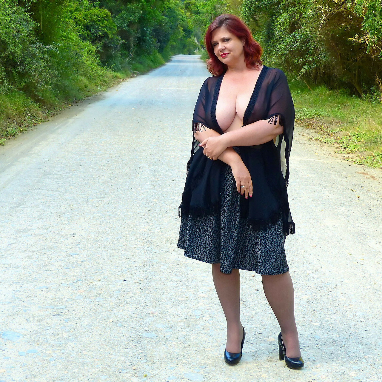 Woman in black dress standing on tree-lined country road