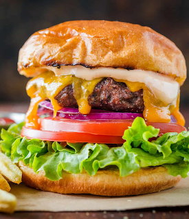 Close-up of a cheeseburger with melted cheese, lettuce, tomato, onion, and sauce on a bun