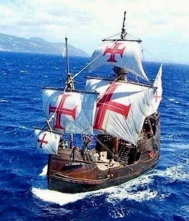 Historic wooden sailing ship with white sails and red crosses on blue ocean