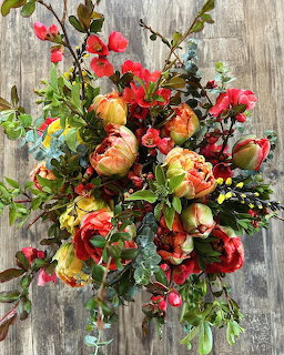 Colorful autumn bouquet with red and peach flowers, greenery, and berries on weathered wood