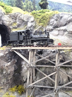 Model steam locomotive on wooden trestle bridge over rocky terrain in miniature railroad layout