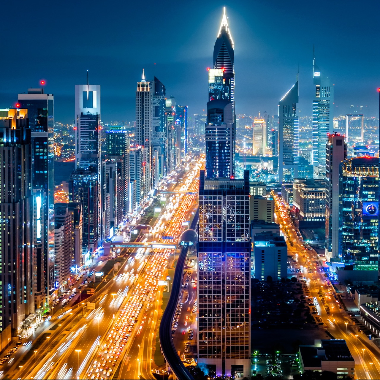 Night skyline of Sheikh Zayed Road in Dubai with lit skyscrapers and glowing traffic trails