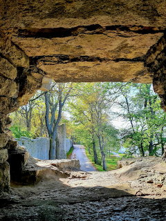 Rocky cave opening framing a dirt path and green trees outside
