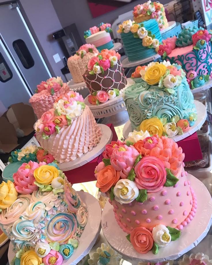 Multiple decorated cakes with colorful buttercream flowers and intricate designs displayed on a table