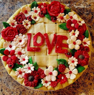 Decorated round pie with red LOVE letters and flower icing on a brown countertop
