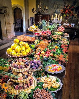 Long banquet table with fruit, pastries, and flowers in a historic hall