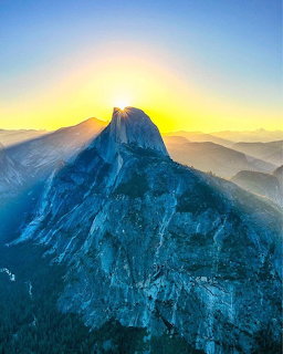 Half Dome granite peak at sunrise with golden sky and layered mountains in Yosemite