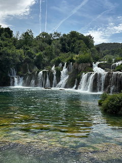 Multiple cascading waterfalls flowing into a clear green pool surrounded by dense green trees