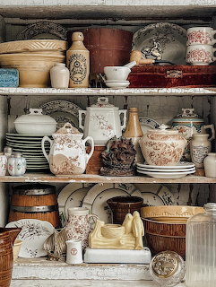 Wooden shelves displaying assorted vintage pottery, teapots, bowls, and ceramic containers in beige and brown tones