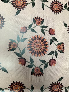 Handmade quilt with central sunflower medallion, tulip wreath, green leaves, and sunflower corner blocks on white background