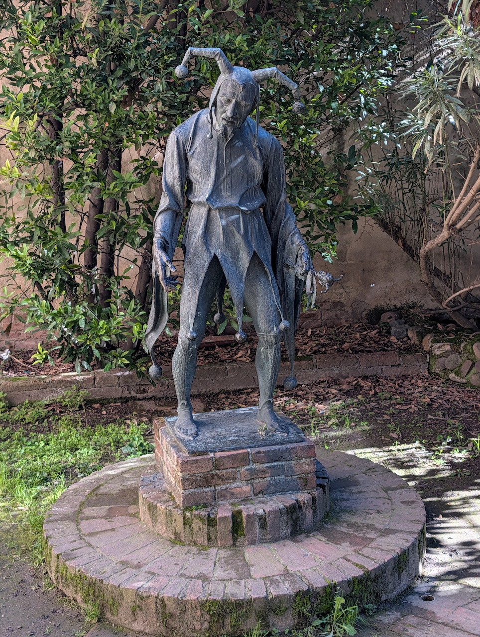 Bronze statue of a man on a round pedestal surrounded by plants in a courtyard