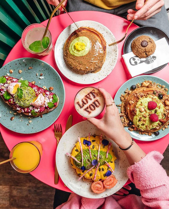Overhead brunch spread with coffee, pastries and fruit on pink background