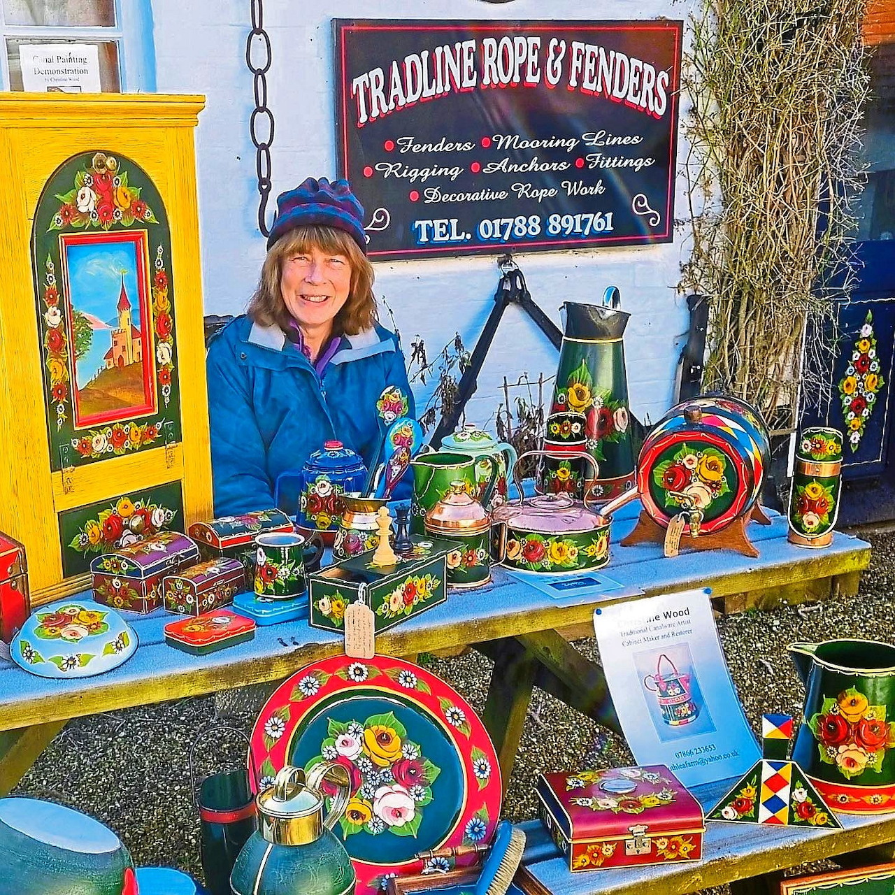 Woman at outdoor market stall displaying colorful hand-painted traditional canalware pottery and decorations