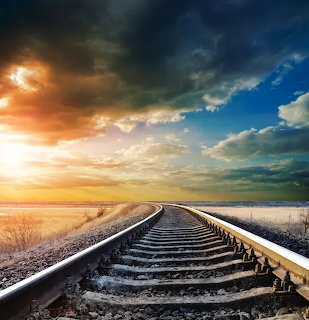 Curving railway tracks under a dramatic sunset sky with clouds