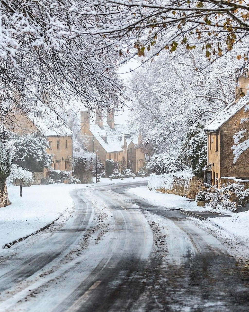Snow-covered village road flanked by stone houses and frost-draped trees in winter
