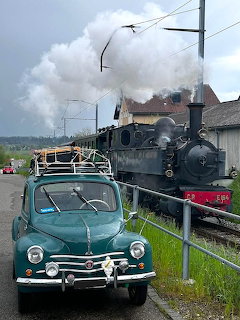 Turquoise vintage car beside black steam locomotive with white smoke