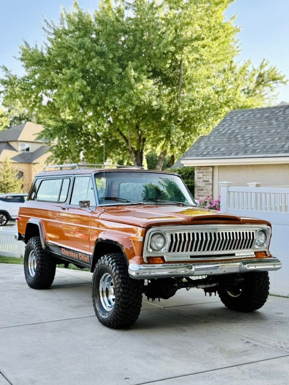 Classic orange and white lifted Jeep Cherokee parked in a suburban driveway with trees in the background