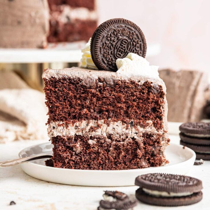 Chocolate cake slice with cream layers and Oreo cookie topping on white plate
