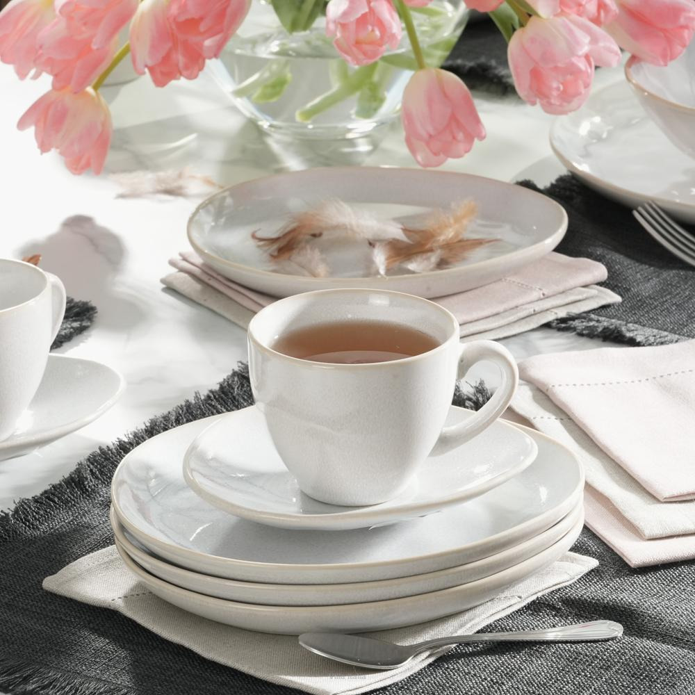 White tea cup on stacked plates with silverware and pink tulips on a bright table